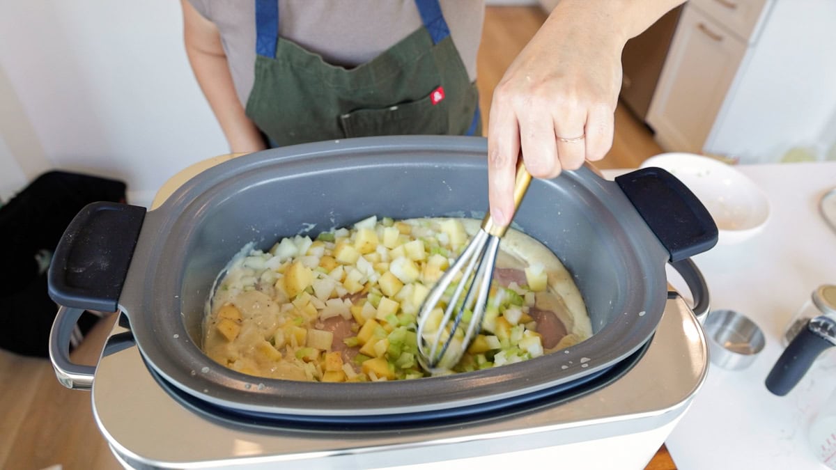 Diced potatoes, chopped onions, and celery added on top of chicken in GreenPan slow cooker for slow cooker chicken pot pie from scratch.