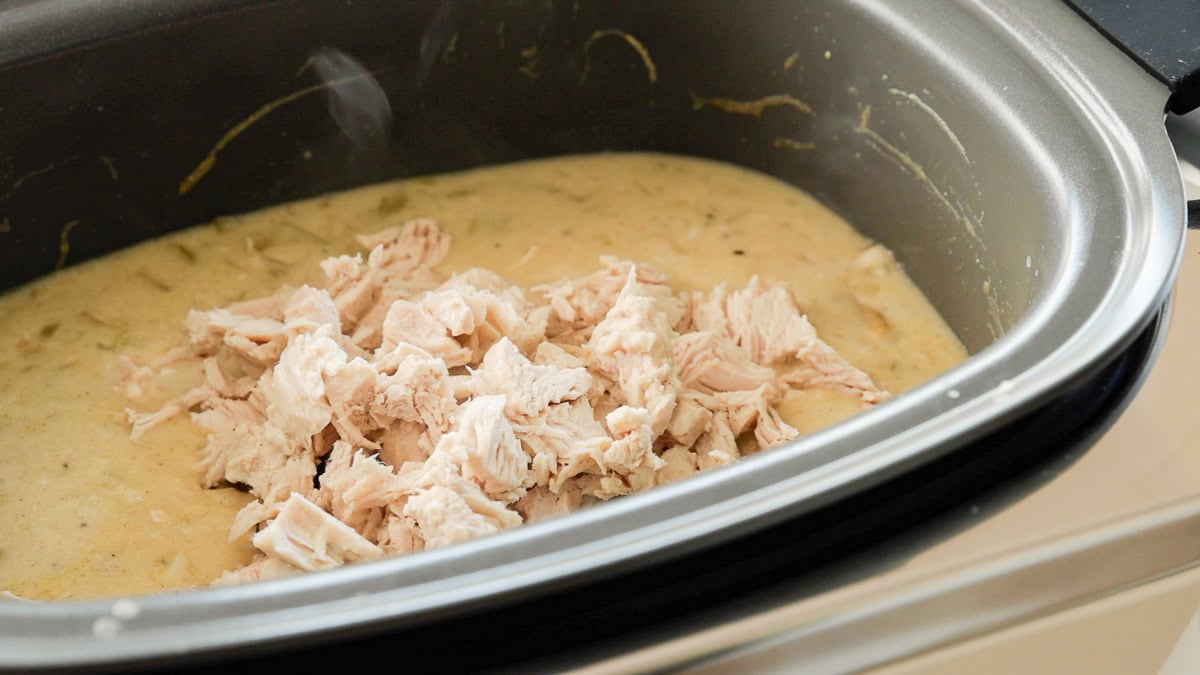 Cooked and diced chicken being added back into creamy slow cooker chicken pot pie from scratch.