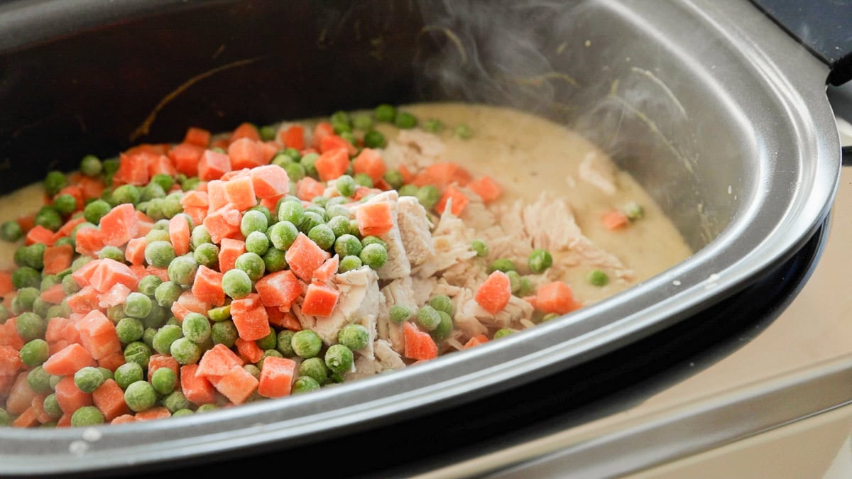 Frozen peas and carrots poured into GreenPan slow cooker with chicken pot pie.