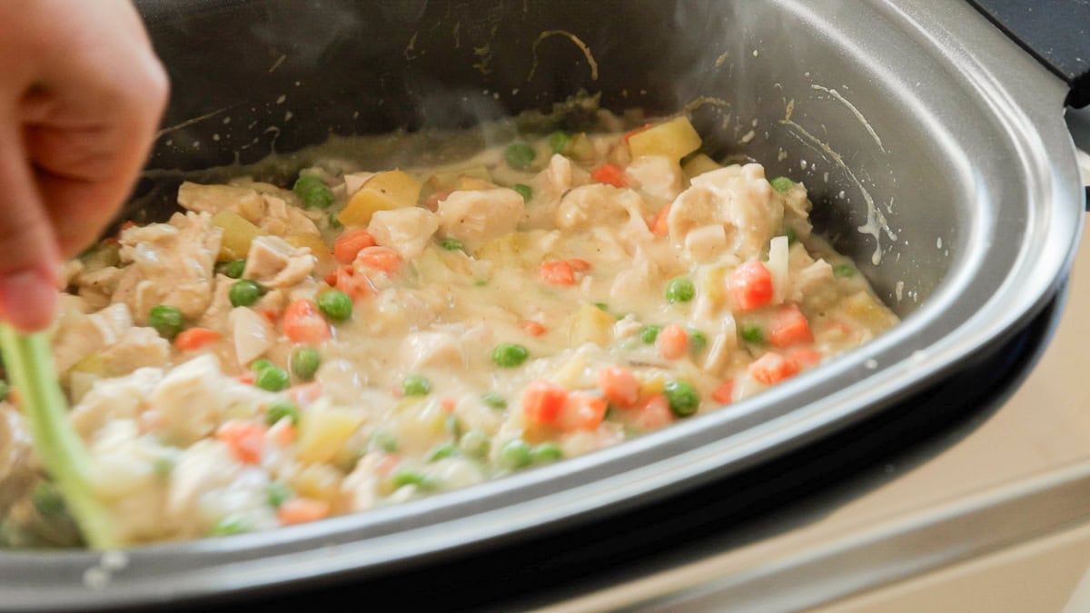 Slow cooker chicken pot pie from scratch being stirred, full of chicken, carrots, peas, and potatoes.