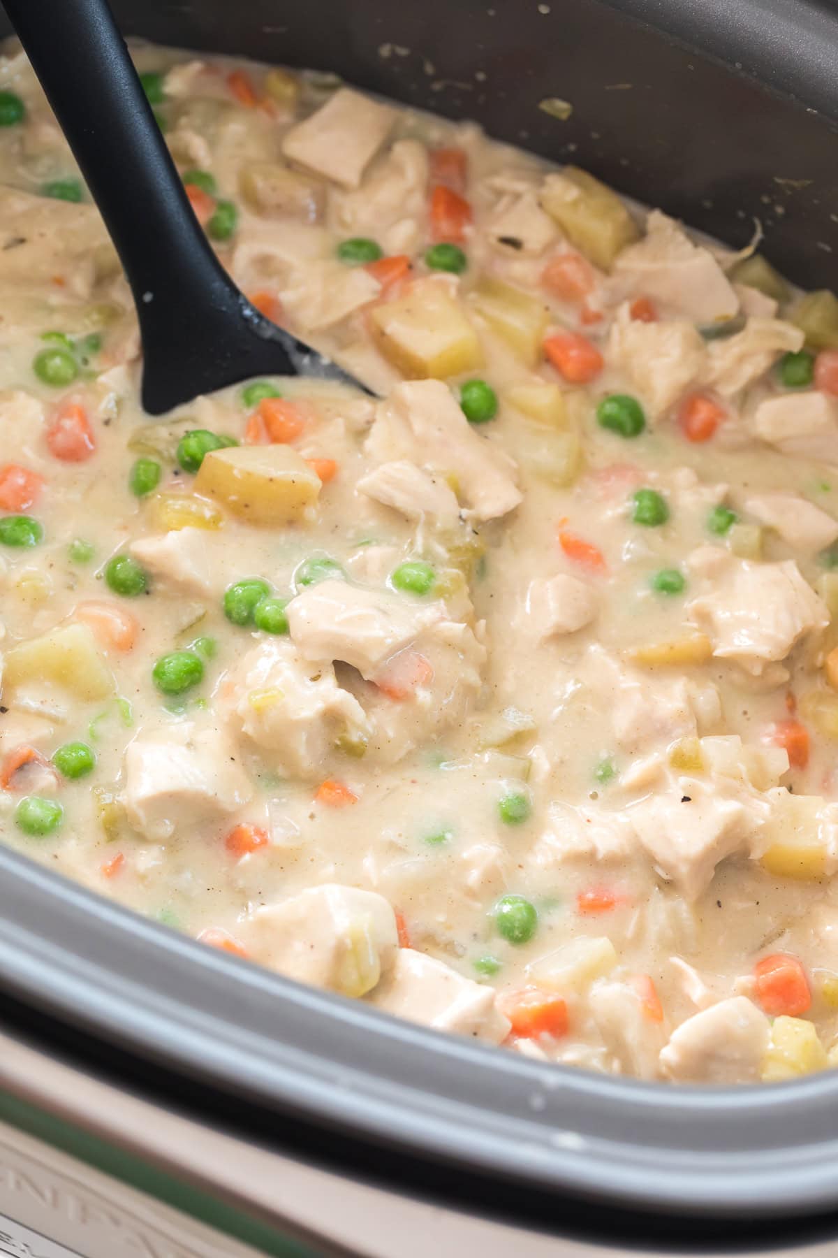 overhead photo of creamy slow cooker chicken pot pie with chicken, carrots, peas, and potatoes.