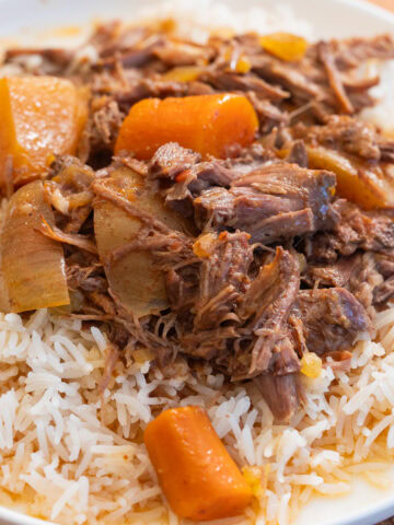 slow cooker pot roast with potatoes and carrots over rice on a white plate.