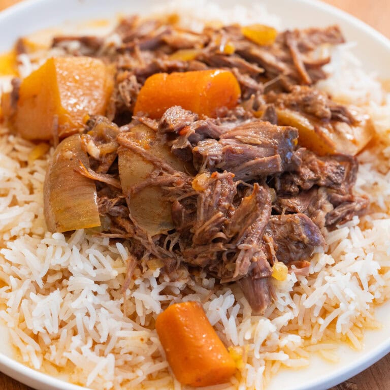 slow cooker pot roast with potatoes and carrots over rice on a white plate.