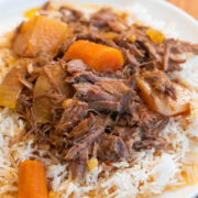 Comforting pot roast with carrots, potatoes, and onions over rice on a white plate.