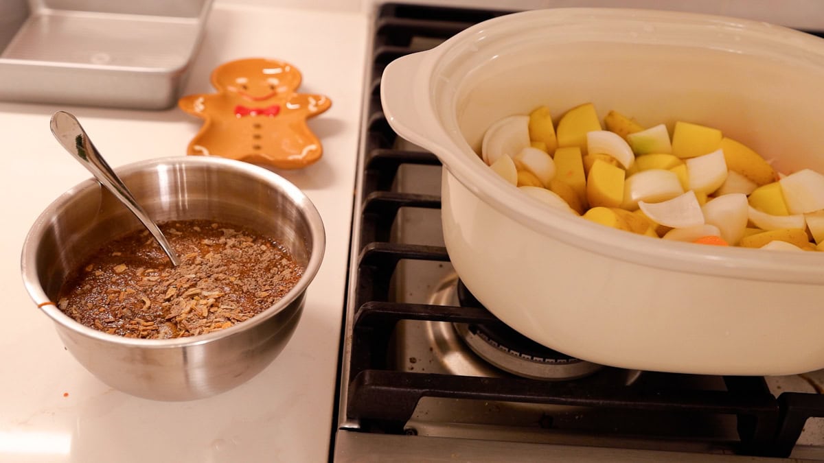 Prepared sauce with onion soup mix in a bowl next to chopped potatoes and onions in a slow cooker.