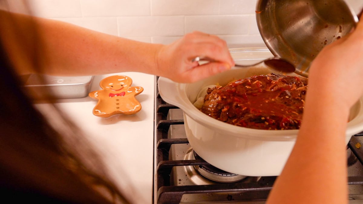 Pouring sauce over a beef roast in a slow cooker with onions and seasonings.