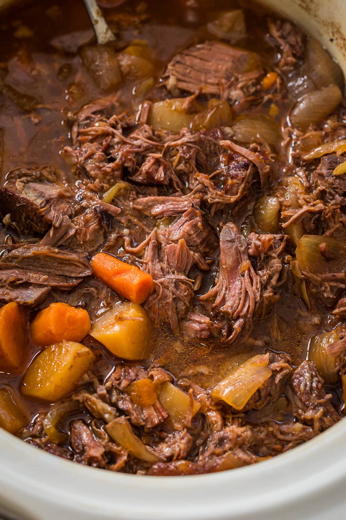 slow cooker filled with pot roast of chuck roast, potatoes, carrots, onions, and a rich sweet flavorful sauce.