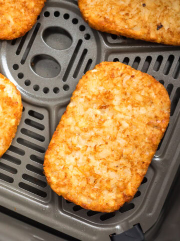 close up photo of air fryer frozen hash browns in air fryer basket.