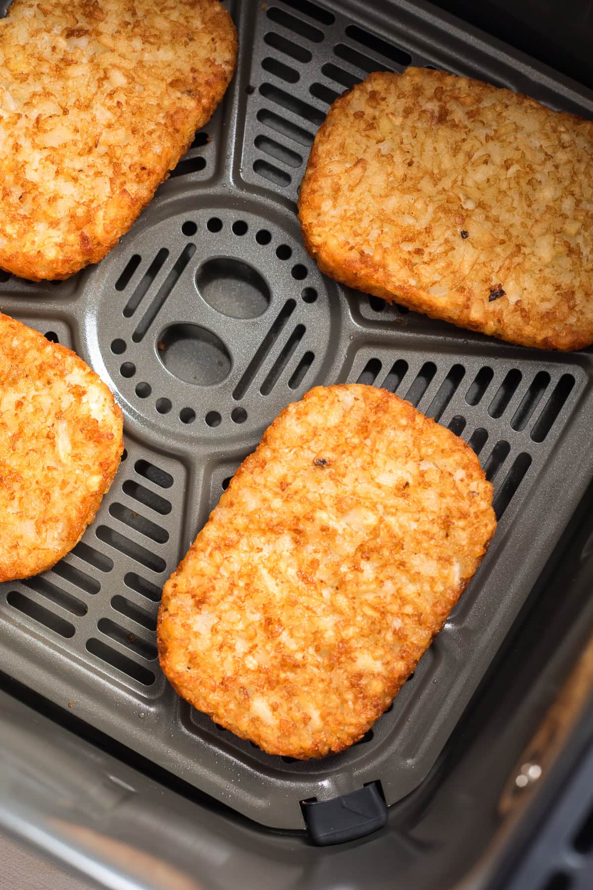 Close-up of hash browns cooking in an air fryer basket.