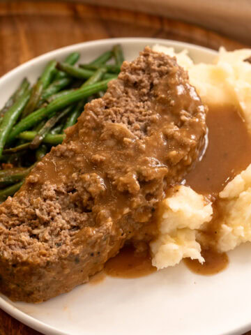 Moist slice of meatloaf topped with brown gravy, served with creamy mashed potatoes and saut&eacute;ed green beans.