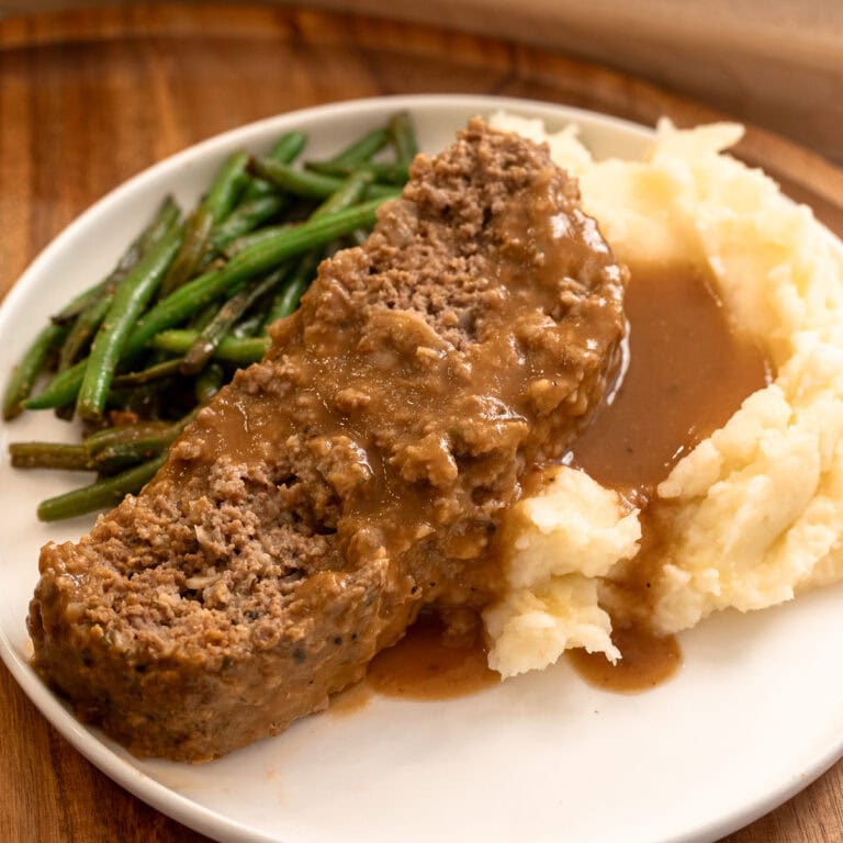 Moist slice of meatloaf topped with brown gravy, served with creamy mashed potatoes and sautéed green beans.