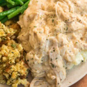 Plate of homemade slow cooker chicken and gravy with green beans and stuffing, showing the thick, creamy texture of the gravy.