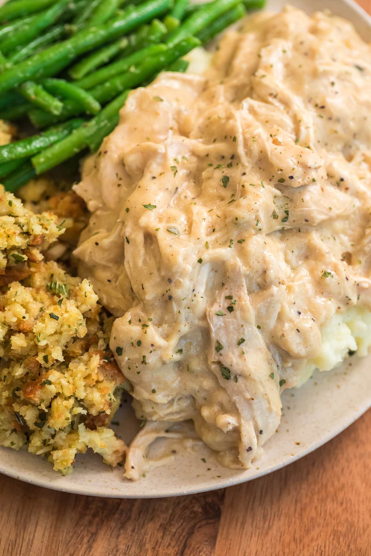 Plate of homemade slow cooker chicken and gravy with green beans and stuffing, showing the thick, creamy texture of the gravy.