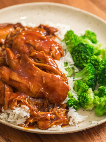 slow cooker honey garlic bbq chicken thighs on a plate with white rice and broccoli.