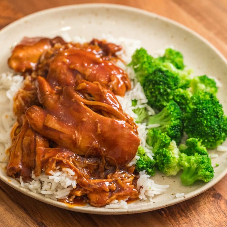 slow cooker honey garlic bbq chicken thighs on a plate with white rice and broccoli.