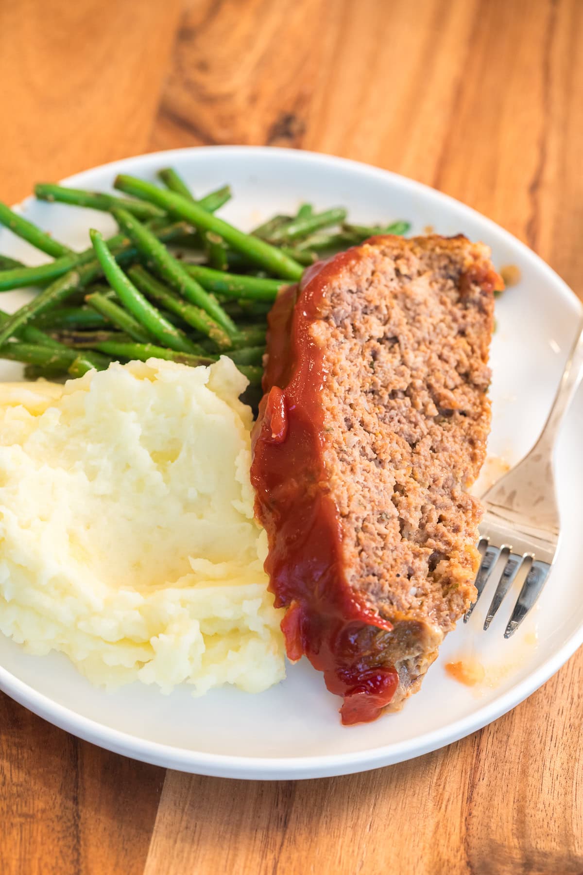 meatloaf on a plate with mashed potatoes and green beans.