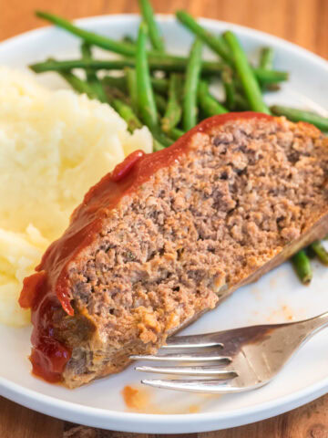 Plated slow cooker meatloaf with mashed potatoes and green beans.