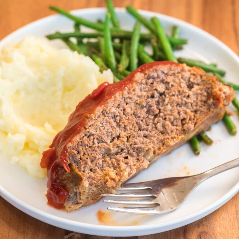 Plated slow cooker meatloaf with mashed potatoes and green beans.