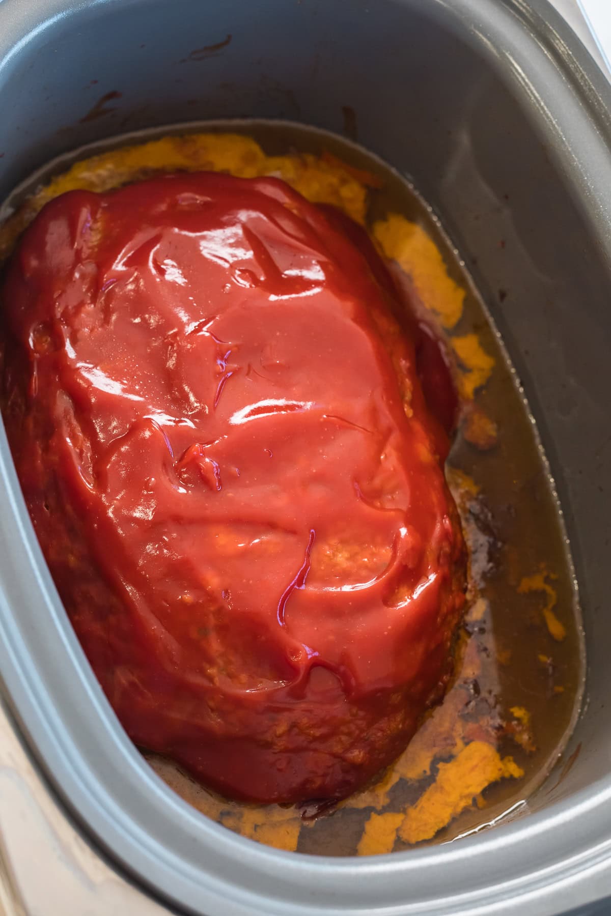 Slow cooker meatloaf with glaze and juices after cooking.