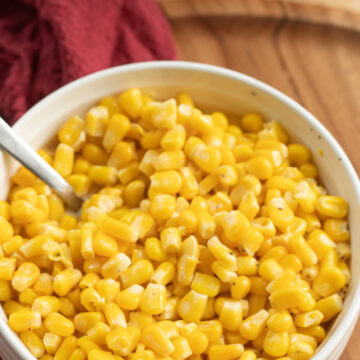 Overhead view of buttered corn served in a bowl with a spoon.