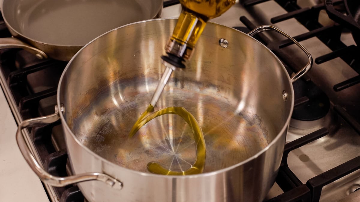 Olive oil being poured into a stainless steel pot on the stovetop.