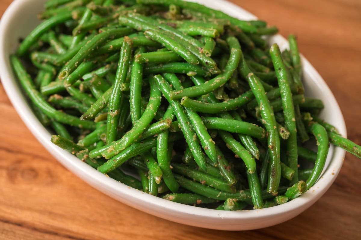 Garlic green beans in a white serving dish, coated lightly with bouillon and seasonings.