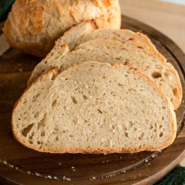 Homemade no knead bread with golden crust and soft crumb, displayed on a wooden surface.