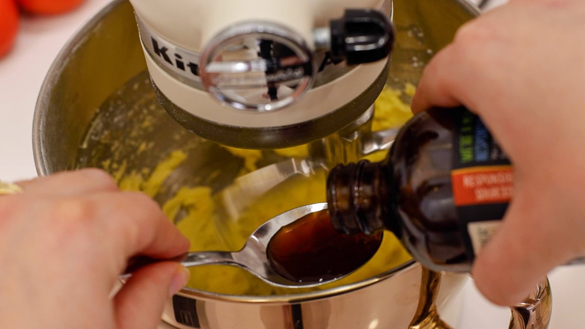 Hands pouring vanilla into spoon to pour into mixing bowl.