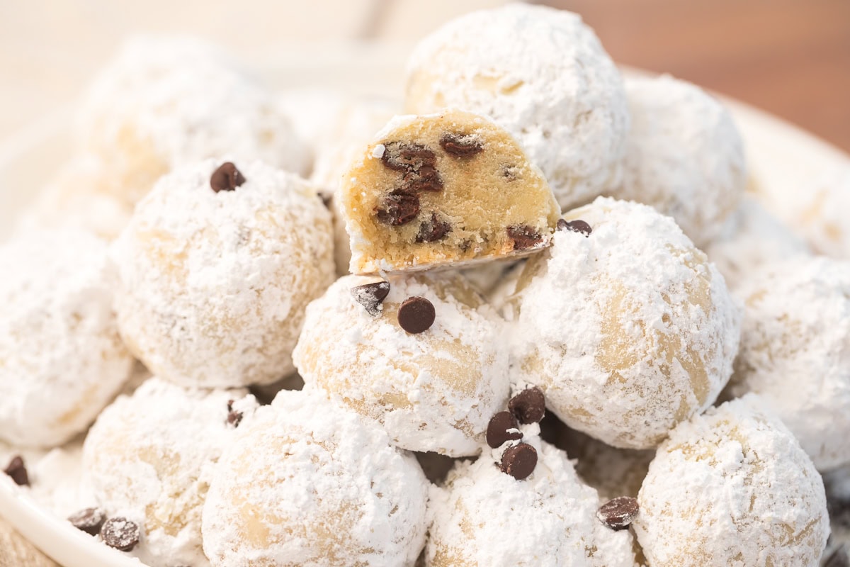 Half of a chocolate chip snowball cookie displayed on top of a cookie pile to show the buttery interior.