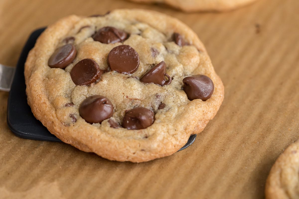 Close-up of a soft and chewy gluten-free chocolate chip cookie loaded with melted chocolate chips on parchment paper.