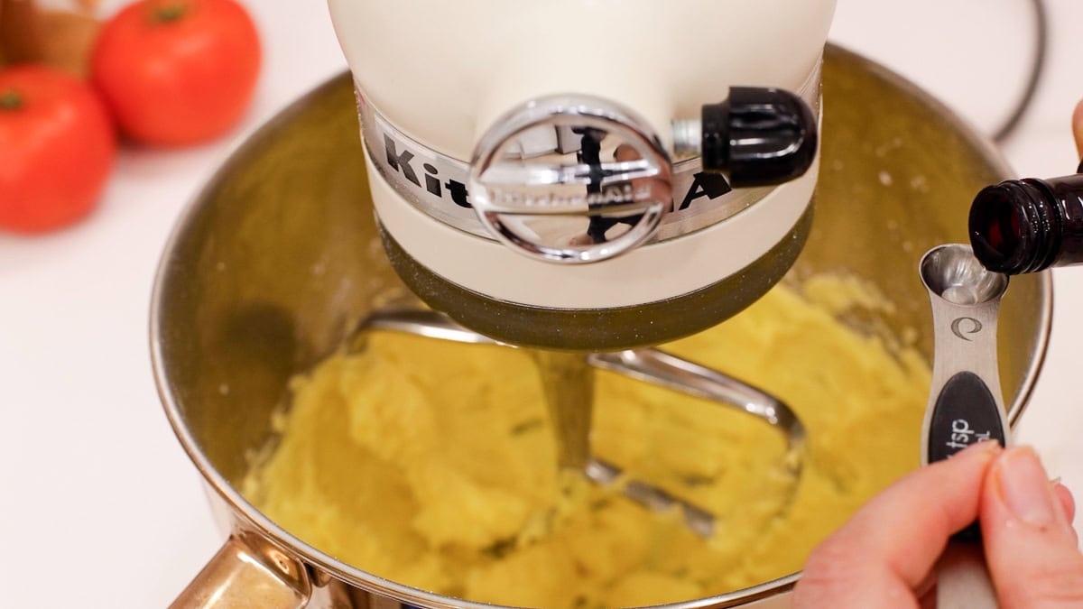 butter mixture in mixing bowl with hands measuring lemon zest into teaspoon.