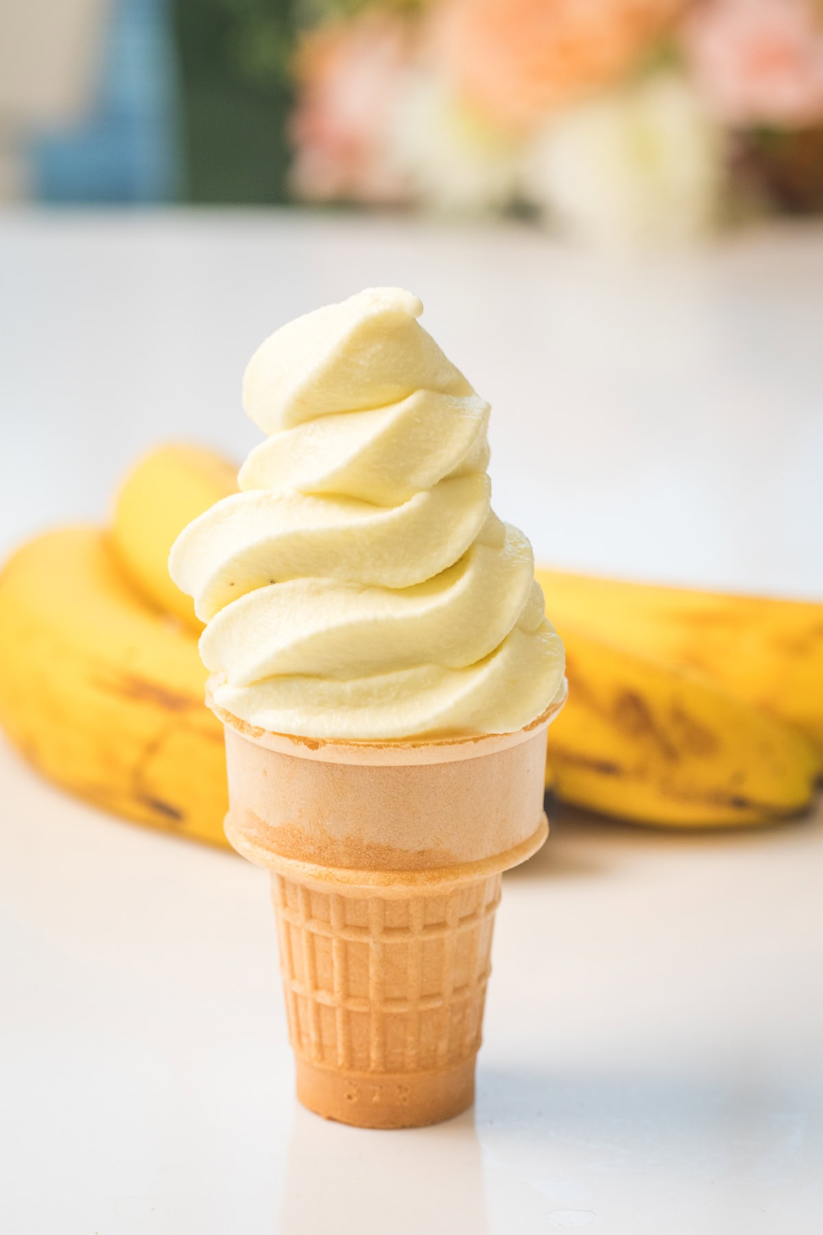 homemade banana soft serve recipe made from the greenpan frost in an ice cream cone with ripe bananas behind it.
