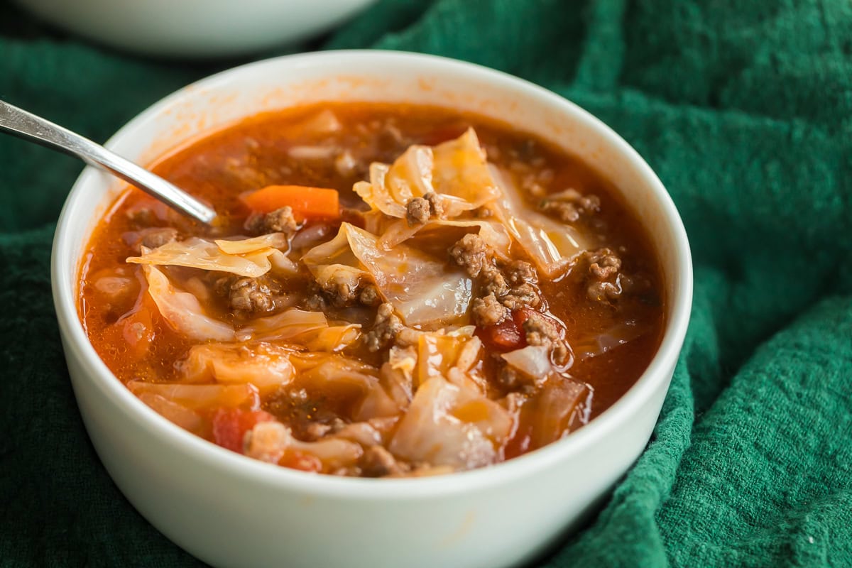 close up of cabbage roll soup in a white bowl on a green napkin.