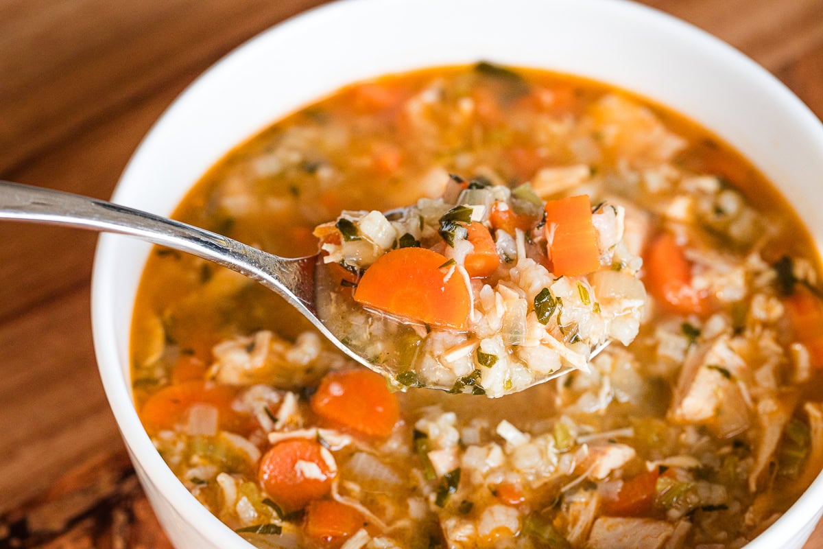 rotisserie chicken and rice soup in a white bowl on a spoon.