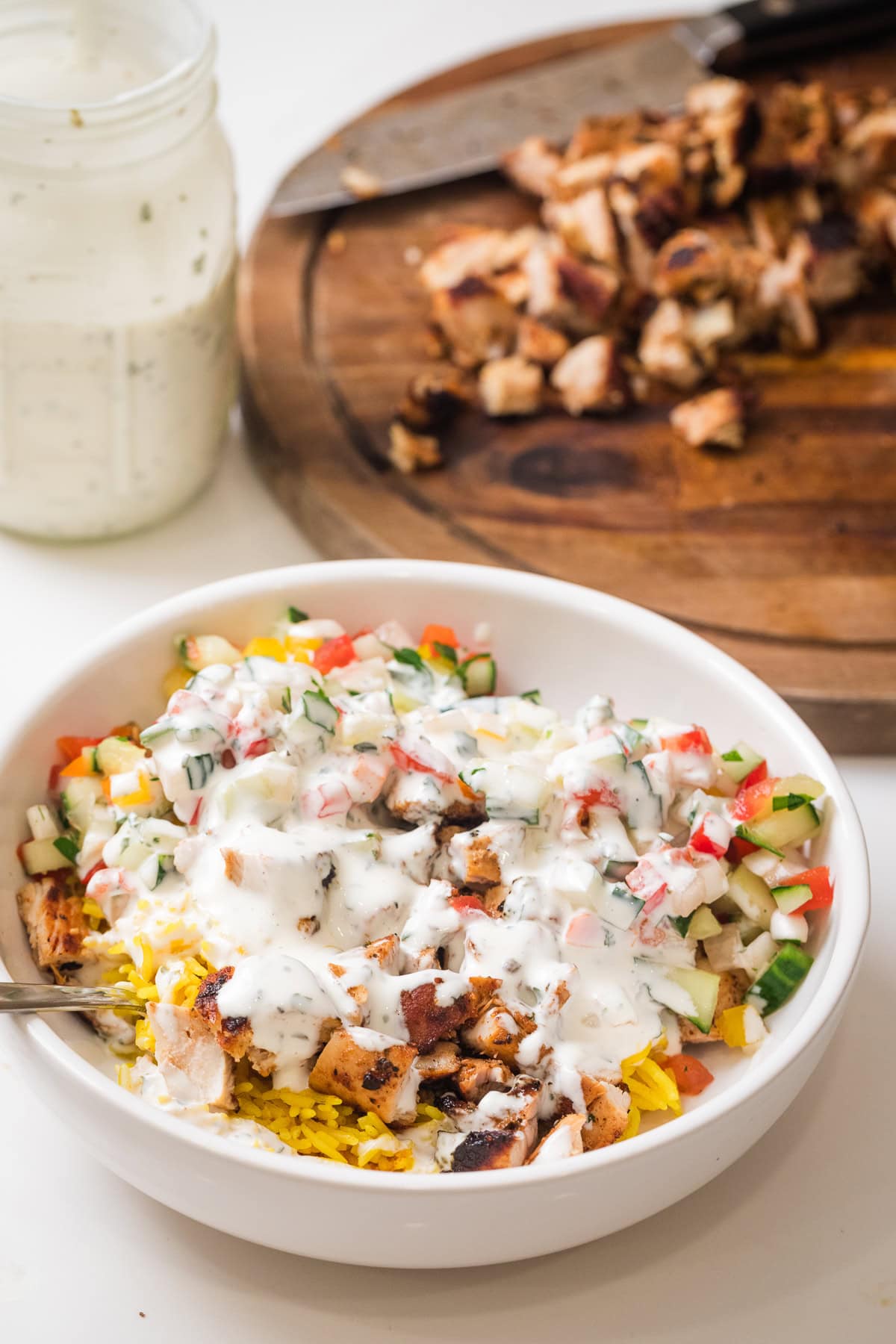 halal cart chicken in white bowl with chicken on cutting board in the background and a container of white sauce.