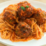 close up of baked chicken meatballs on a plate with spaghetti and sauce.