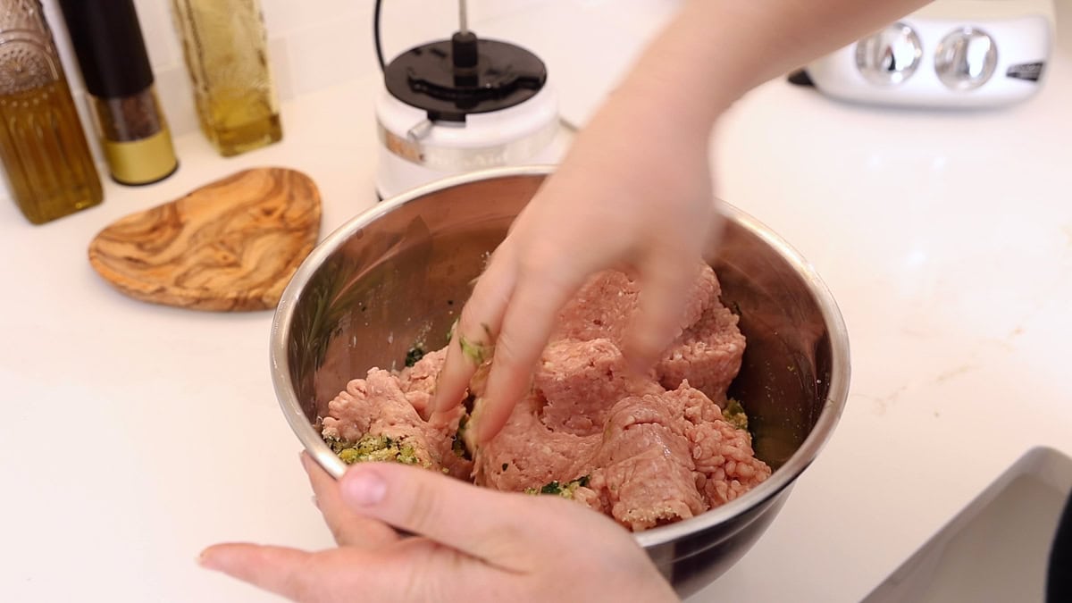 hands mixing chicken meatballs in a big stainless steel bowl.