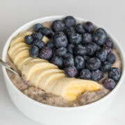 Close-up of a creamy oat bran breakfast bowl topped with neatly sliced banana and a generous layer of fresh blueberries in a white bowl.