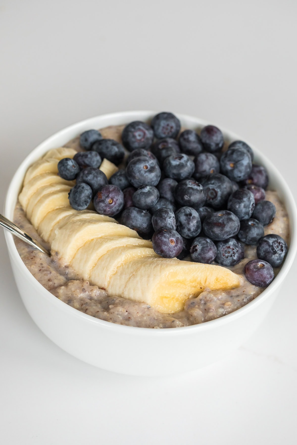 Close-up of a creamy oat bran breakfast bowl topped with neatly sliced banana and a generous layer of fresh blueberries in a white bowl.
