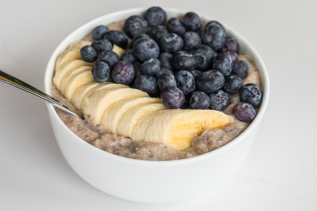 A high-fiber oat bran bowl with banana slices and fresh blueberries, showing the thick, creamy texture.