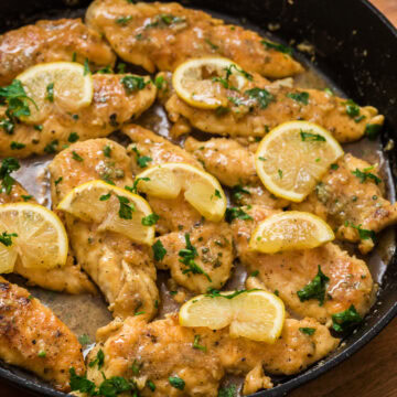 Close-up of lemon garlic chicken tenderloins simmering in a skillet with fresh lemon slices and parsley.