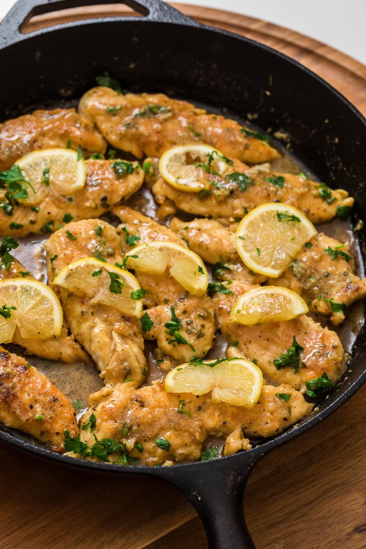 Close-up of lemon garlic chicken tenderloins simmering in a skillet with fresh lemon slices and parsley.