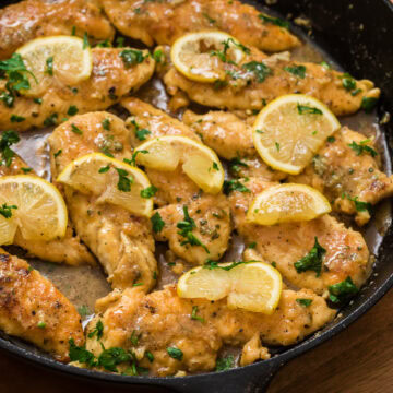 Lemon garlic chicken in a cast iron skillet with lemon slices and fresh parsley garnish.