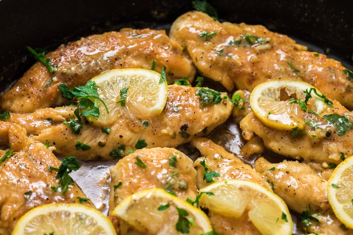 Lemon garlic chicken tenderloins in a skillet with lemon slices and fresh parsley in a buttery garlic sauce.