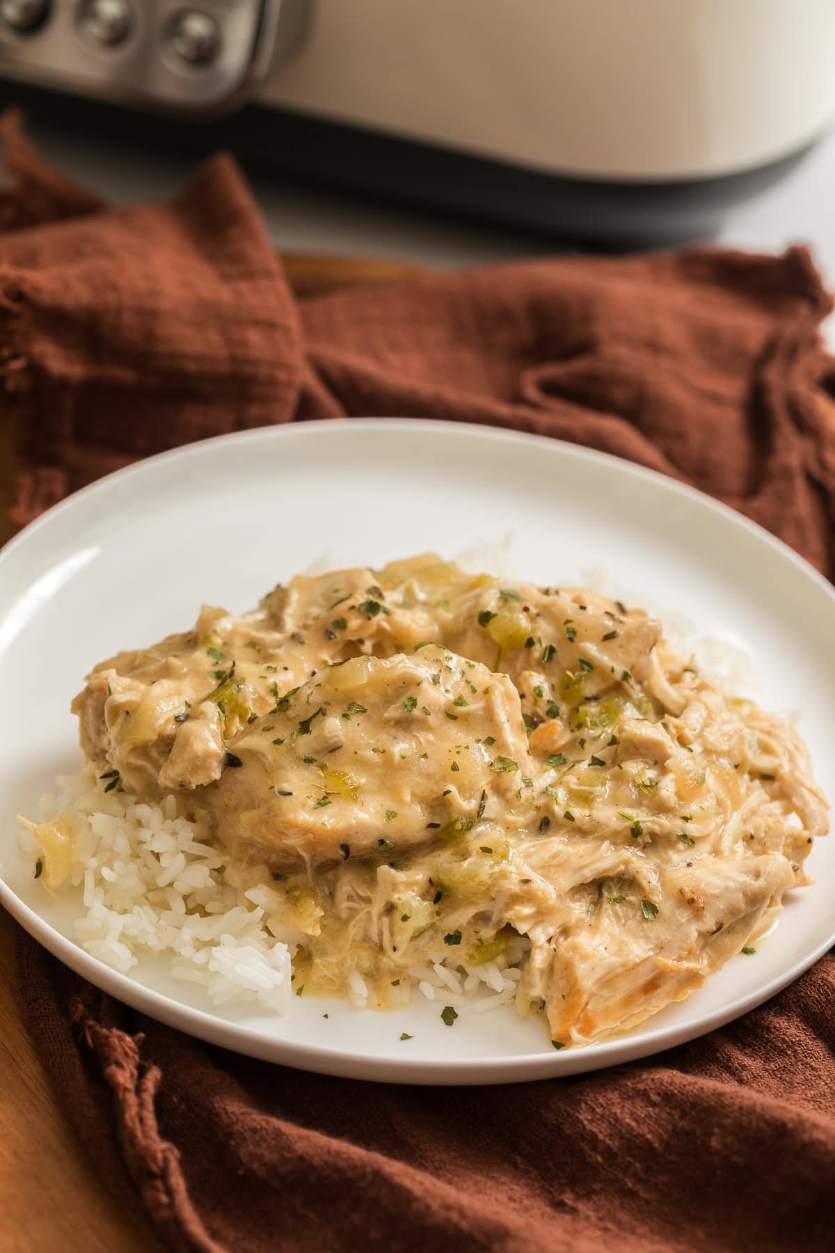 Homemade slow cooker creamy chicken served over white rice on a white plate.