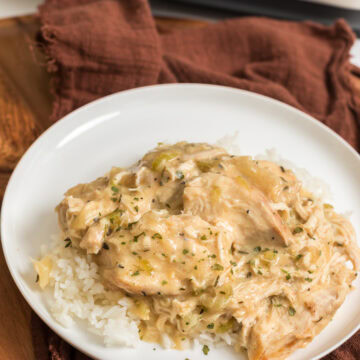 Creamy slow cooker chicken over jasmine rice with a crockpot in the background.