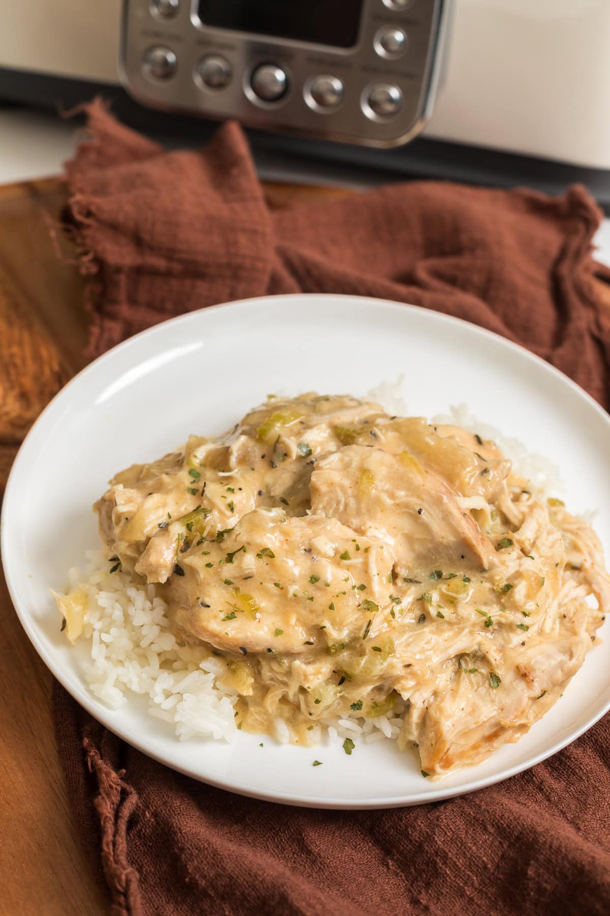 Creamy slow cooker chicken over jasmine rice with a crockpot in the background.