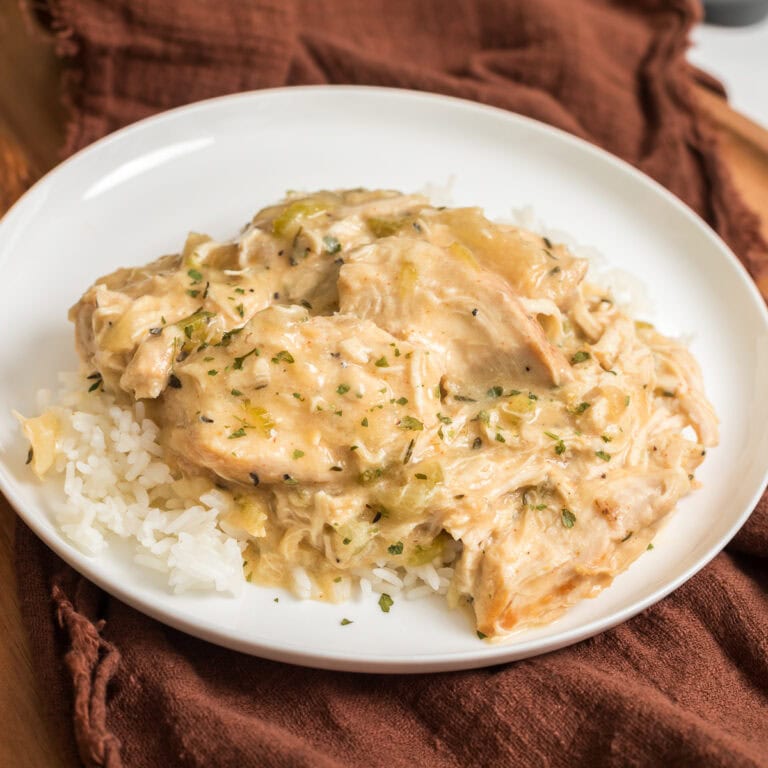 Slow cooker creamy chicken served over jasmine rice on a white plate with a brown napkin.
