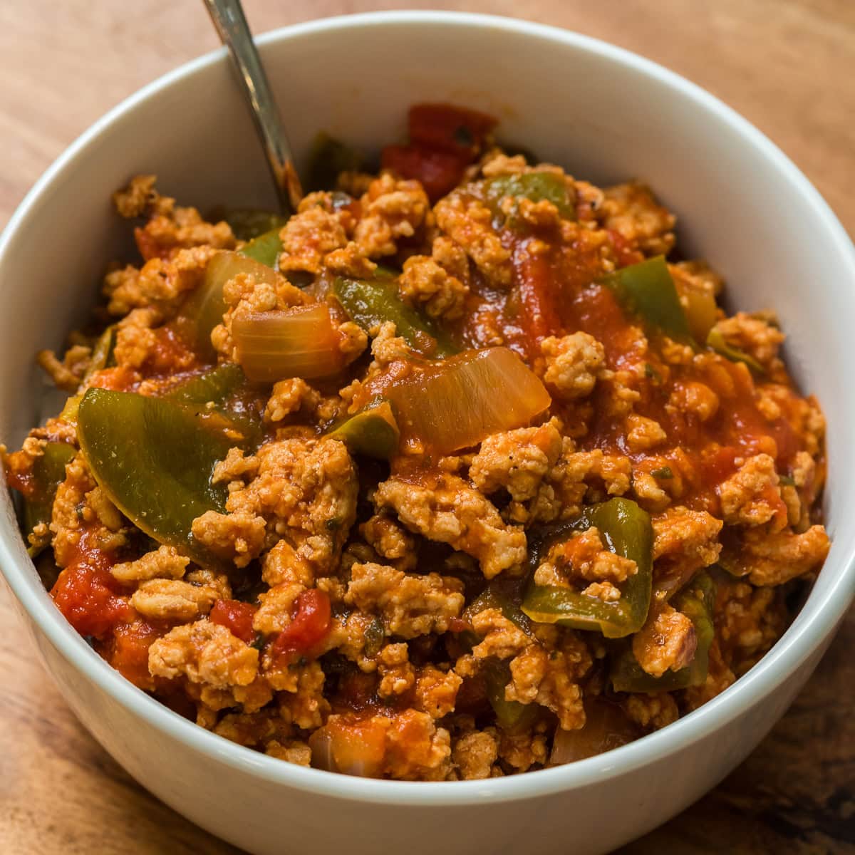 Bowl of ground chicken unstuffed peppers with green bell peppers, onions, and tomato sauce.