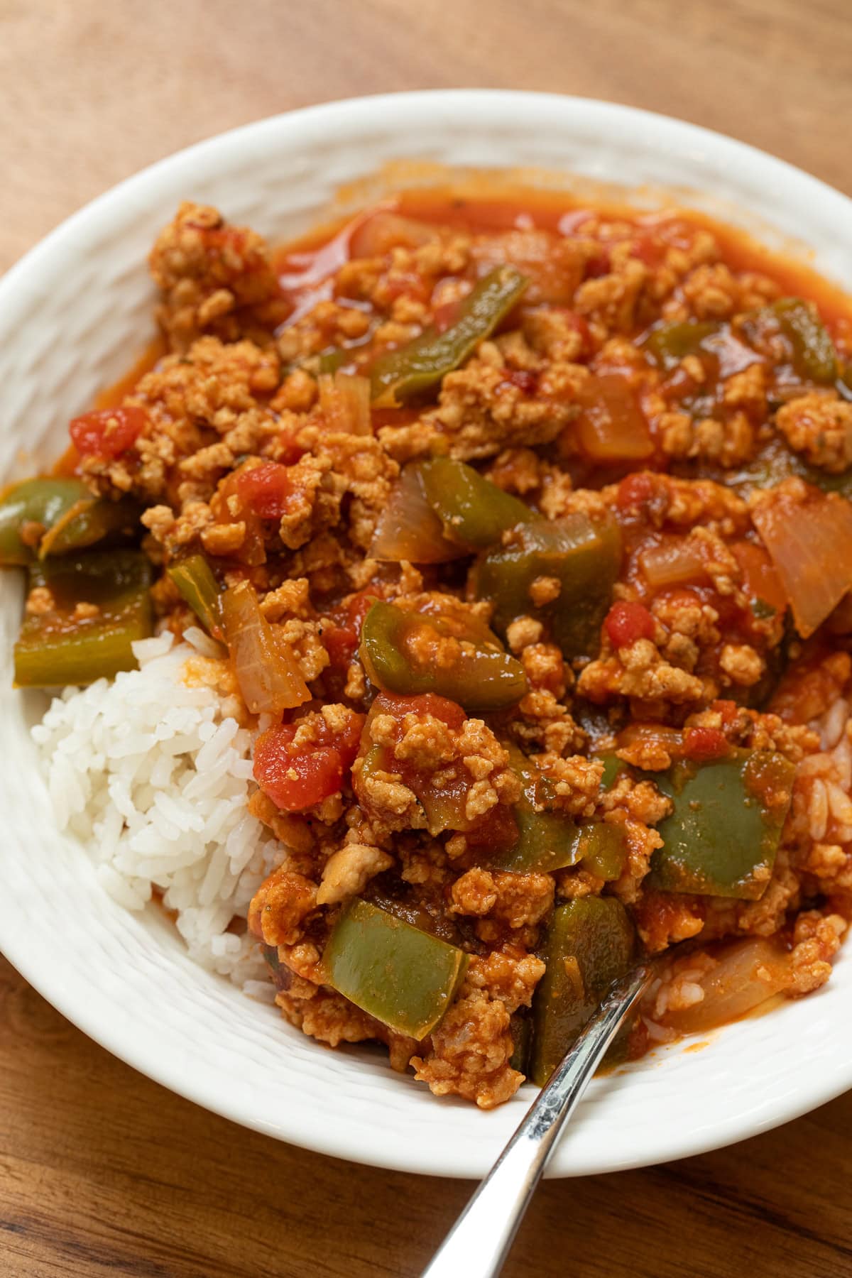 Unstuffed peppers made with ground chicken, green bell peppers, onions, and tomato sauce served over white rice in a bowl.